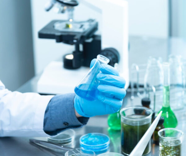 a person in a lab coat and gloves holding a flask of blue liquid