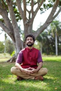 a man sitting in the grass in front of a tree