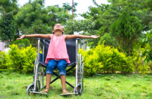 a little girl sitting in a wheel chair in the grass